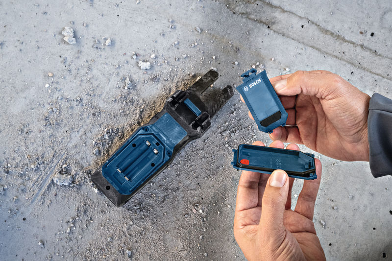 Person, die auf einem staubigen Betonboden eine Batterie in der Basis eines Elektrowerkzeugs austauscht. Anwendungsbild
