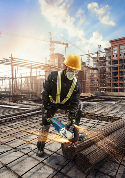 Eine Person mit Sicherheitsausrüstung verwendet einen Winkelschleifer, um auf einer Baustelle Bewehrungsstahl zu schneiden. Anwendungsbild Weitwinkelaufnahme
