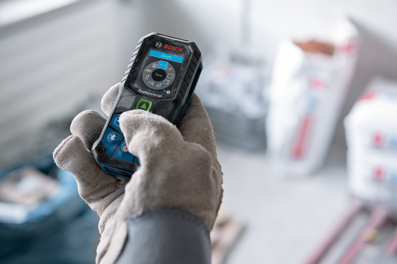 Eine Person mit Sicherheitsausrüstung bedient ein Lasermessgerät auf einer Baustelle. Anwendungsbild