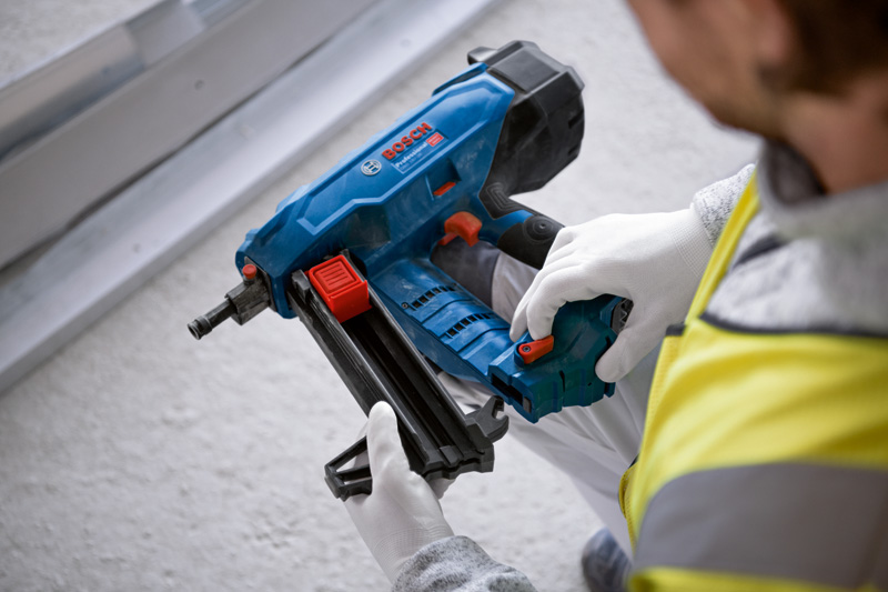 Eine Person mit Sicherheitsausrüstung lädt Nägel in einen blauen Akku-Betonnagler. Anwendungsbild
